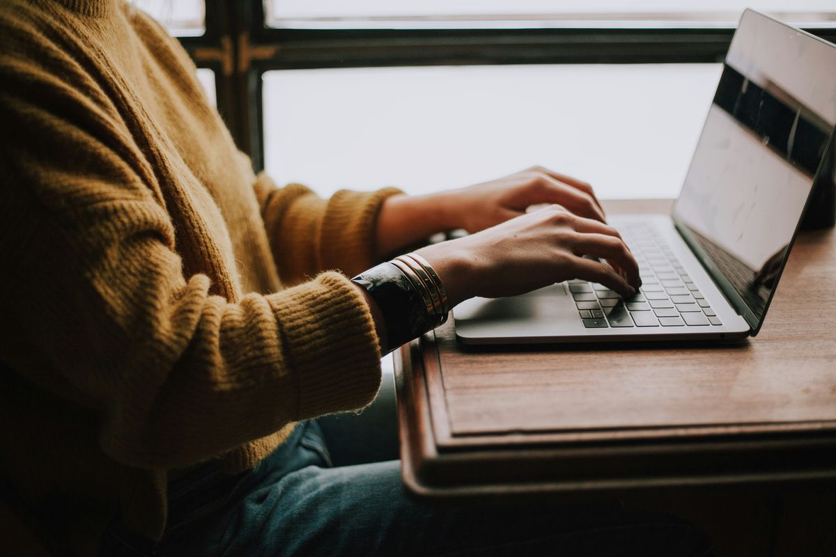 A person typing on a laptop at a desk by a window
