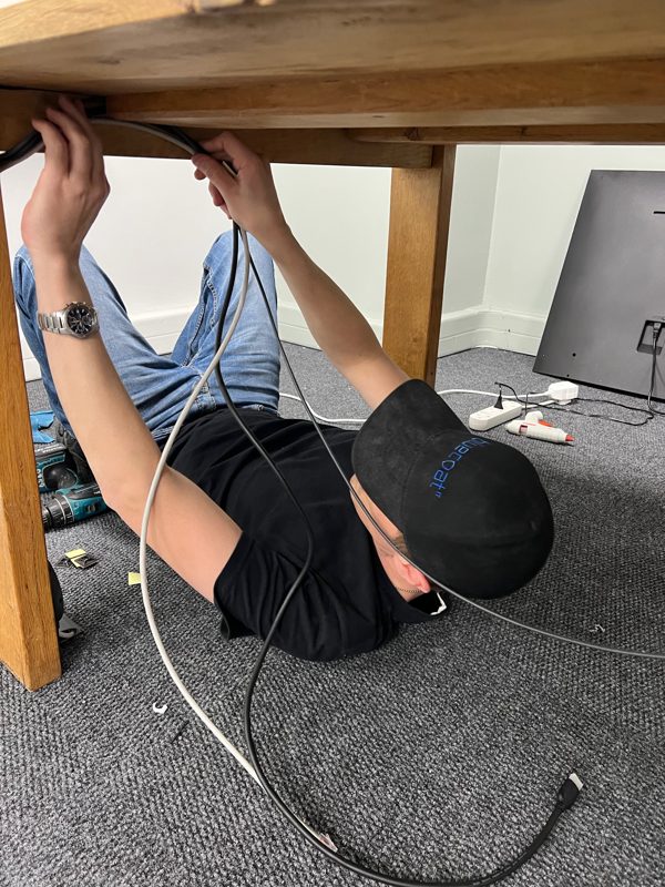 A bluecoat IT technician lying under a boardroom table running cables