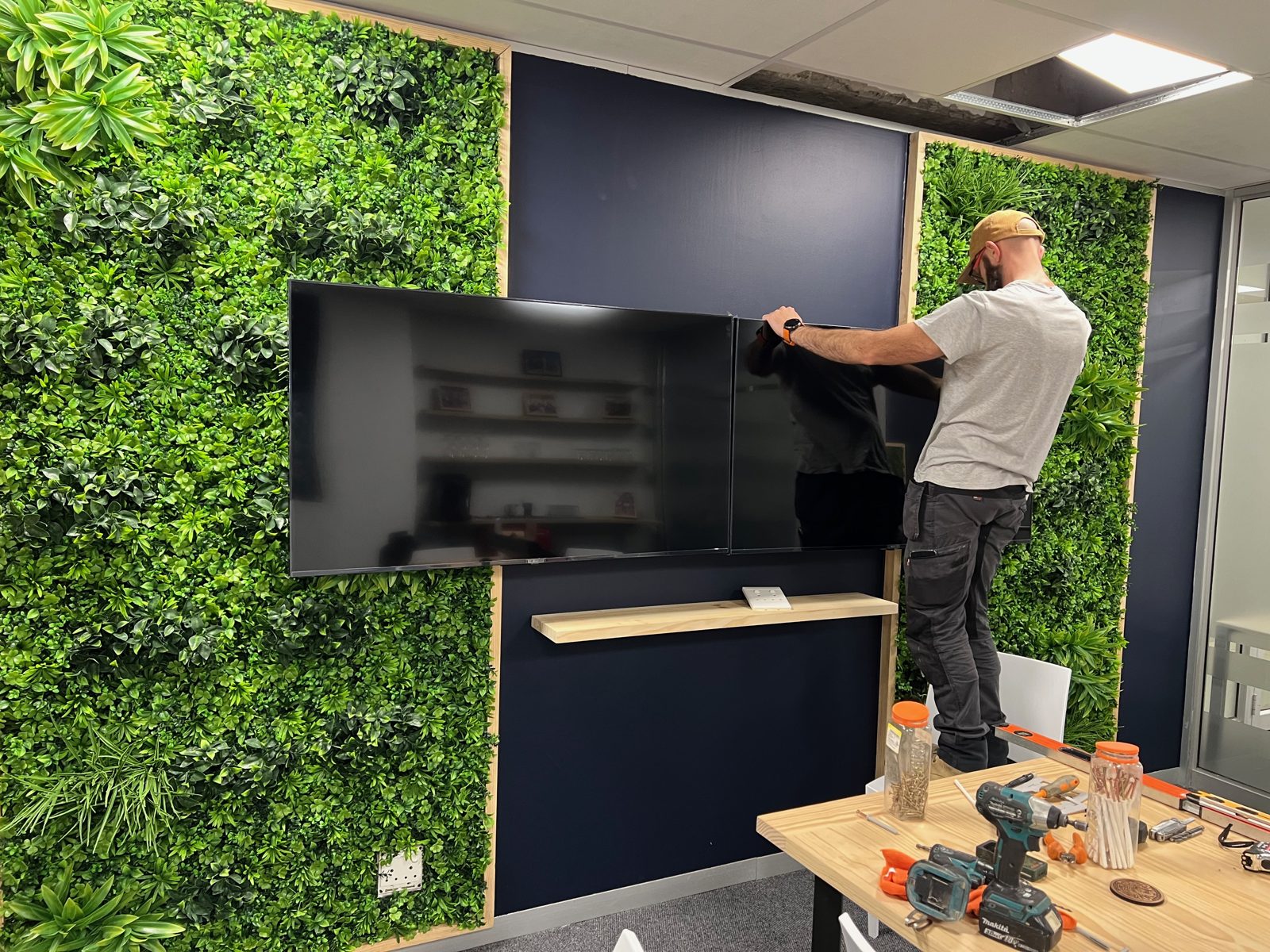 A bluecoat IT technician lifting a large screen into a wall bracket