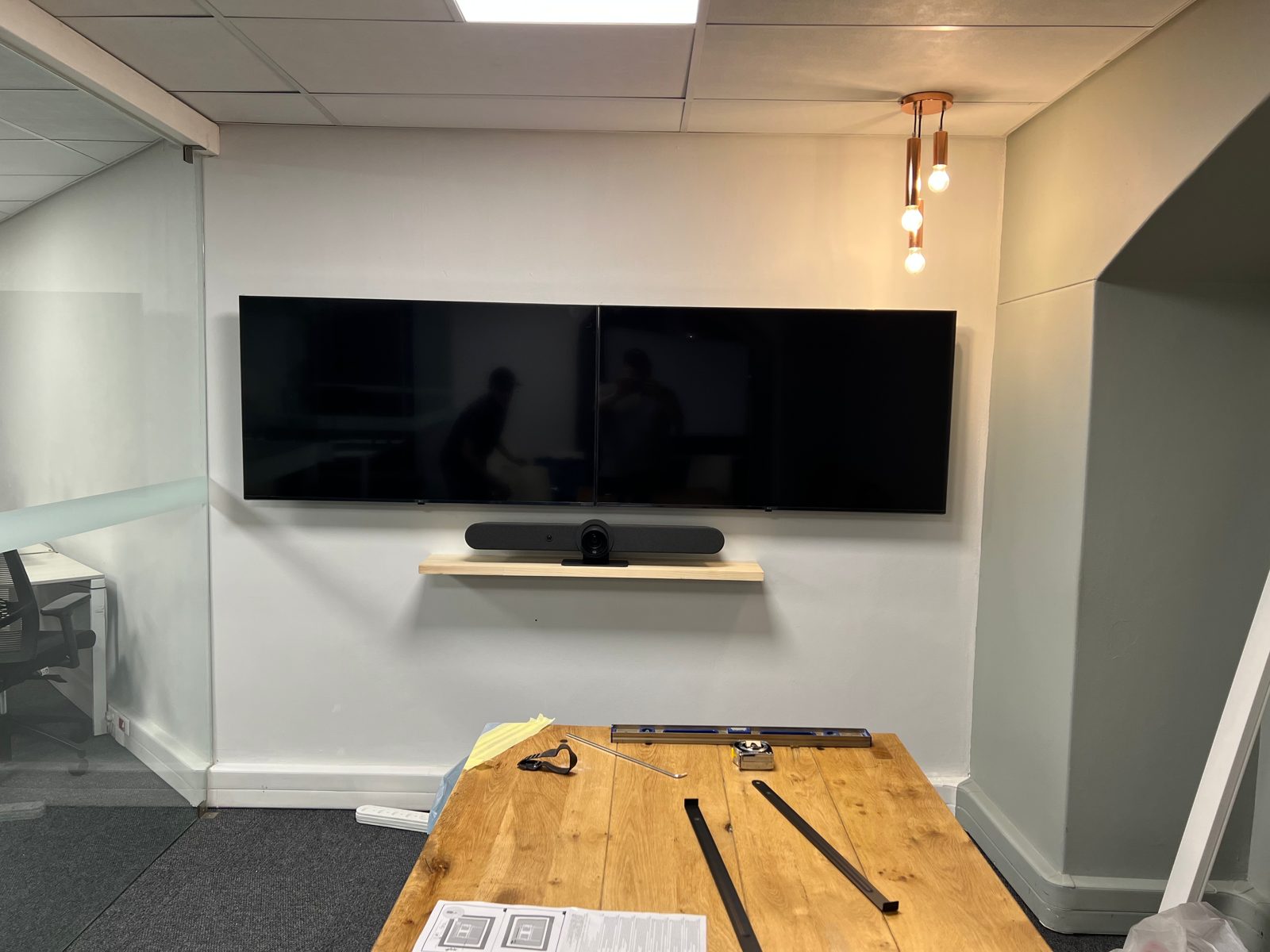 A finished meeting room with two wall-mounted screens and a video bar on a shelf below them